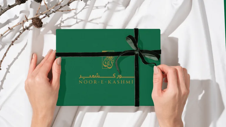 Hands tying a ribbon around a deep green gift box